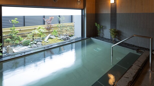 Une piscine intérieure moderne, dotée d’une paroi en verre, de murs recouverts de panneaux en bois et offrant une vue sur un jardin.