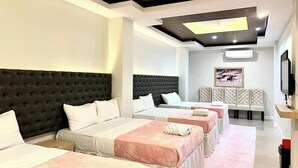 A hotel room with multiple beds, a large headboard, a flat-screen TV, and a ceiling with recessed lighting. - Seacliff Suites Hotel & Resort (Pinamalayan)