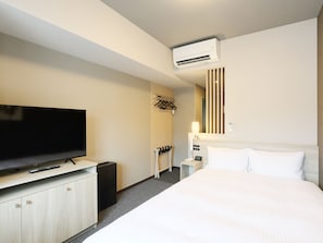 A hotel room with a bed, a TV, a wardrobe, a mirror, and an air conditioning unit.