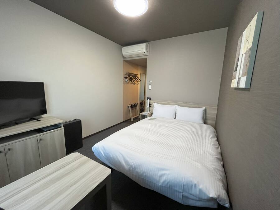 A hotel room with a bed, a TV, a desk, and a wardrobe.