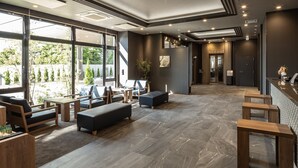 A modern hotel lobby with seating areas, a reception desk, and large windows offering views of greenery. - Hotel Route Inn Imabari (Imabari)