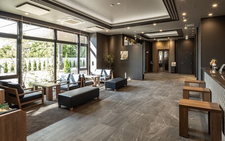 Un moderno vestíbulo de hotel con zonas de estar, un mostrador de recepción y grandes ventanales con vistas a zonas verdes.