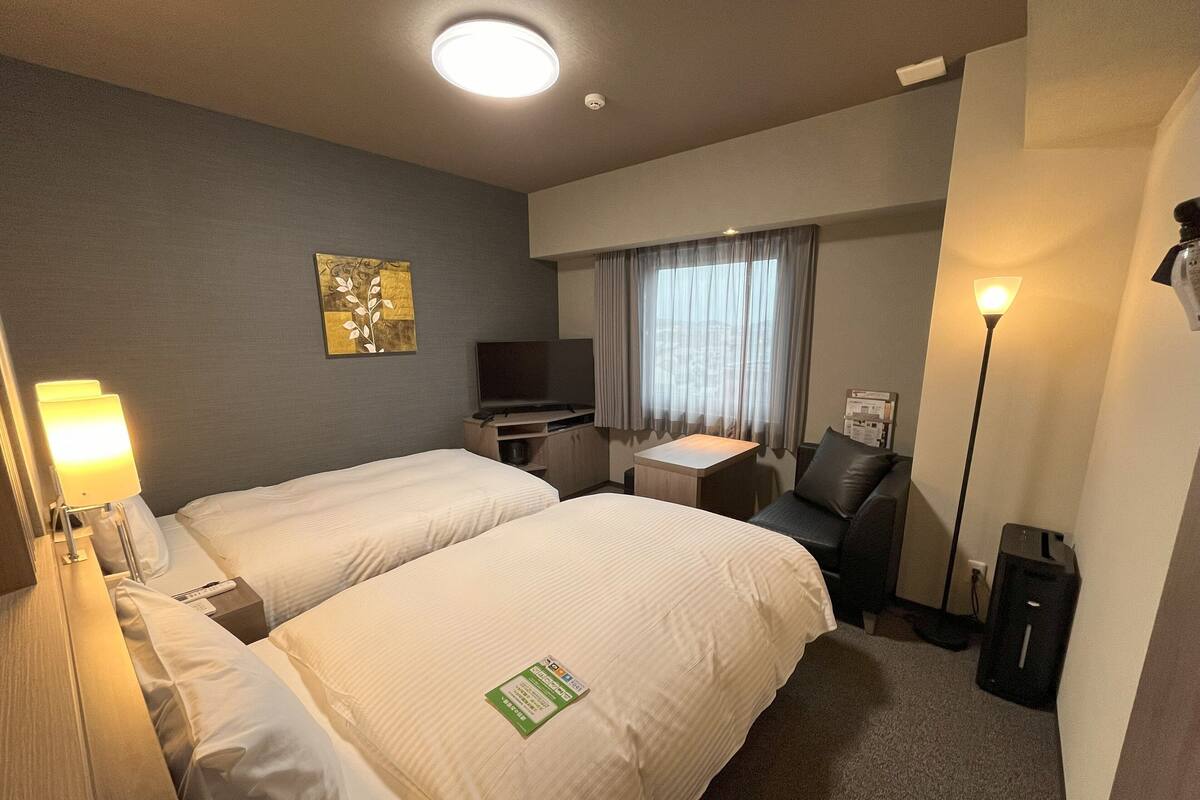Habitación de hotel con dos camas, un escritorio, una silla, un televisor y una lámpara.