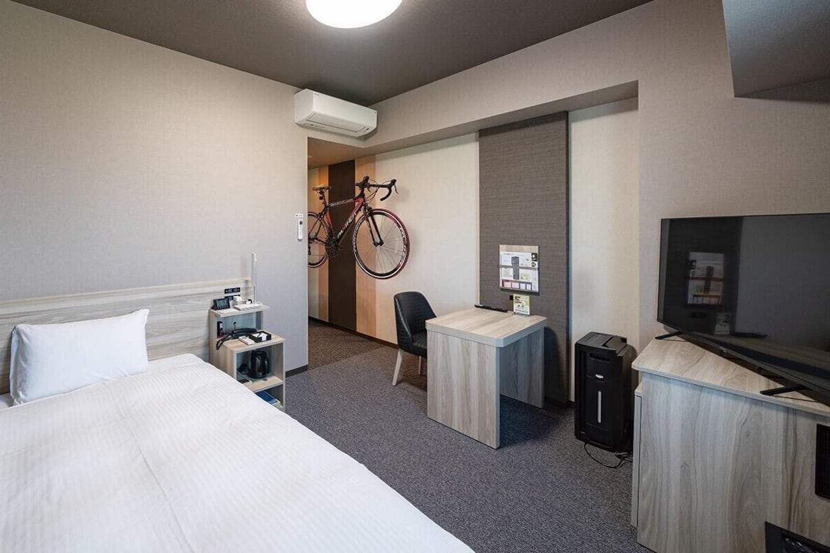 Habitación de hotel con cama, escritorio, silla, televisión, estacionamiento para bicicletas y un minibar.