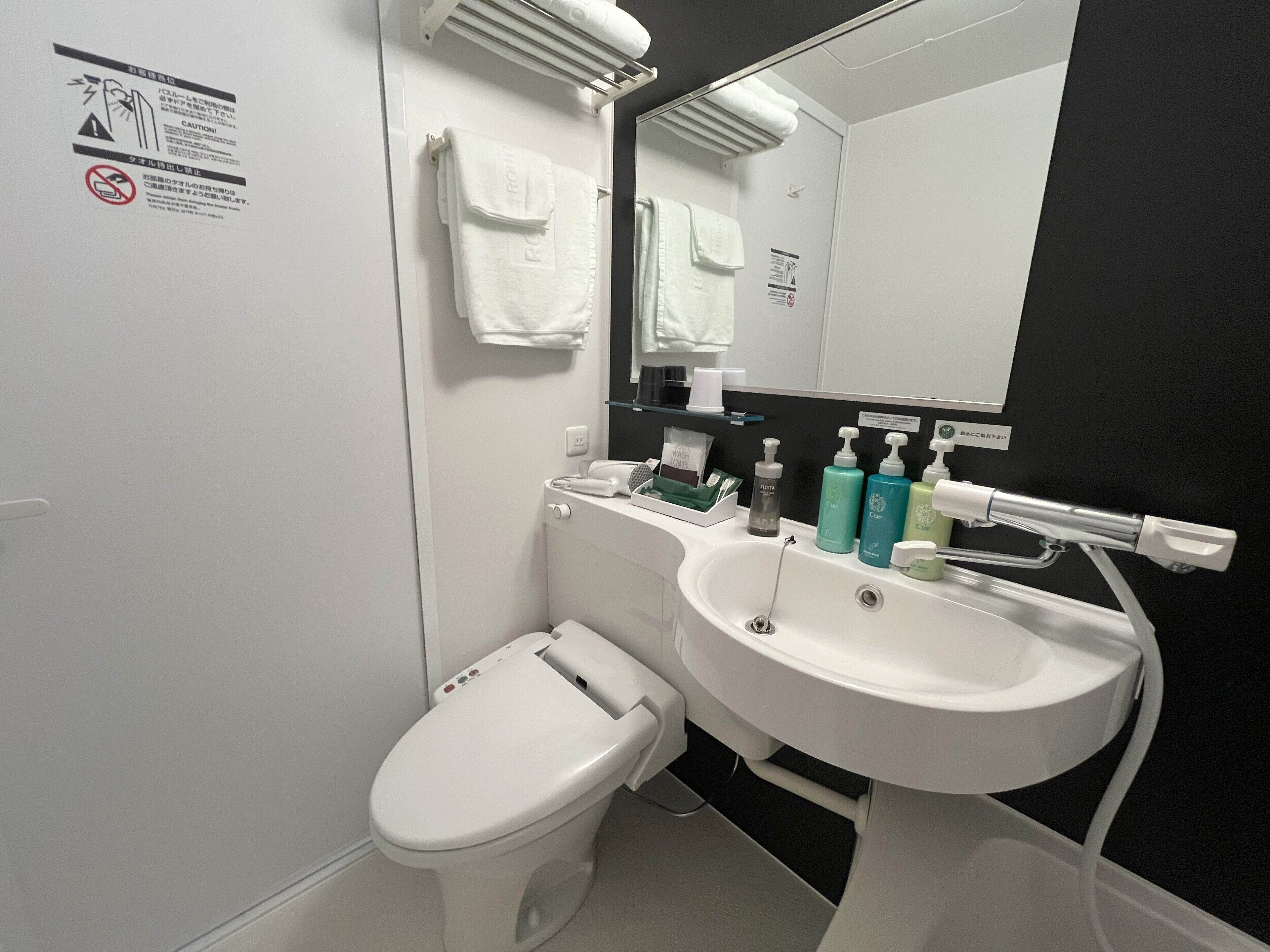 A modern bathroom with a white toilet, a sink, and a mirror. There are toiletries on the sink counter.