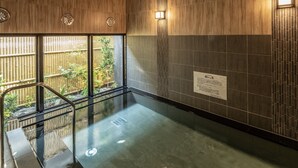 Un área de piscina interior moderna con una barrera de vidrio, paredes de paneles de madera y vistas a un jardín de bambú.