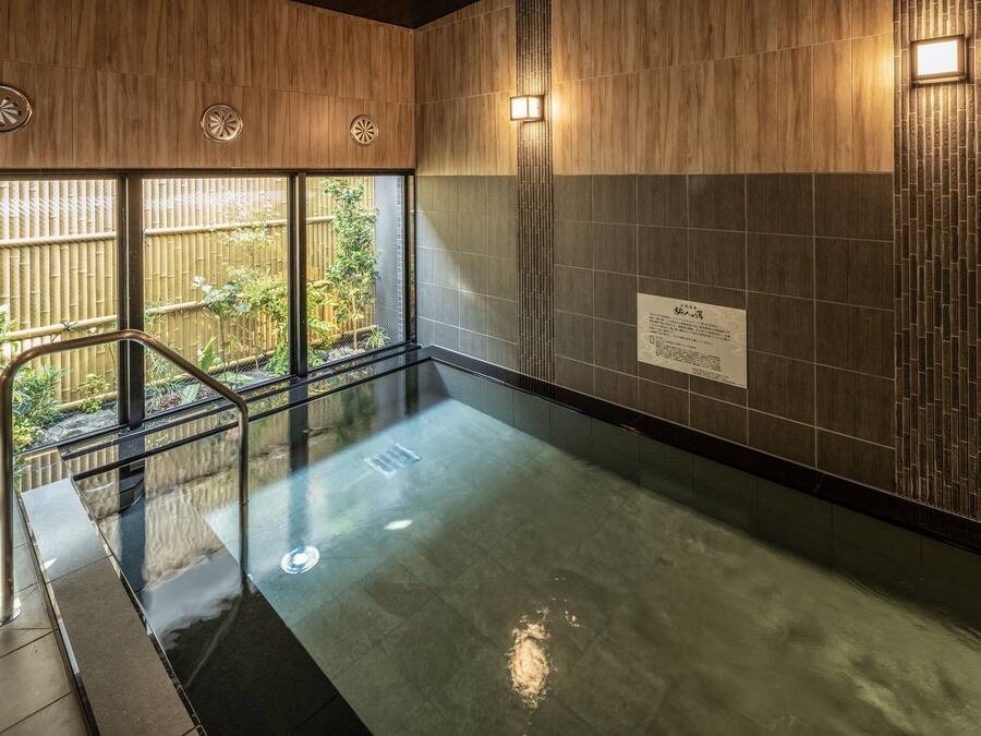 A modern indoor pool area with a glass barrier, wooden panel walls, and a view of a bamboo garden.