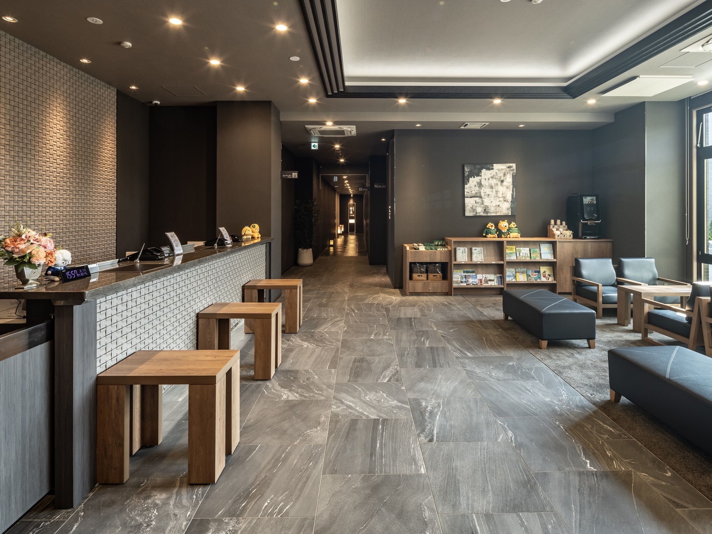 A modern hotel lobby with a reception desk, seating area, and a bookshelf.