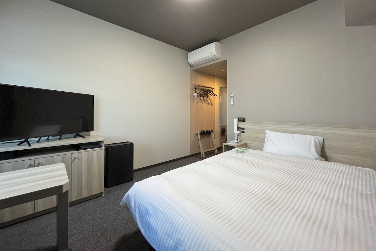 Una habitación de hotel con una cama, televisión, escritorio y armario.