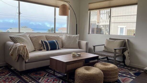 Un salon chaleureux avec un canapé, un fauteuil, des poufs, une table basse et un tapis à motifs.