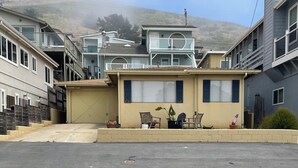 Une maison d’habitation avec un garage, deux fenêtres et un petit porche agrémenté de chaises et de plantes en pot.
