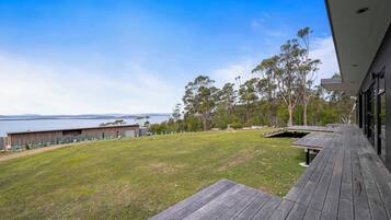 A modern building with a wooden deck overlooking a grassy area and a body of water.
