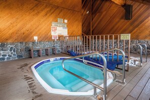 Piscina interior com parede de pedra e teto de madeira, cercada por grades de metal e bancos.