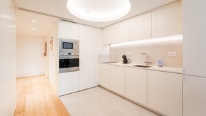 Uma cozinha moderna com armários brancos, forno embutido, máquina de café e um grande lustre circular.