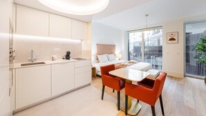 Une chambre d’hôtel moderne dotée d’un coin cuisine, d’une table à manger avec des chaises, d’un lit avec une tête de lit et d’un balcon avec vue.