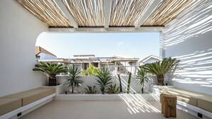 A modern outdoor patio with a white wall, a wooden ceiling, and a view of neighboring buildings. - Villa Tora Canggu (Canggu)