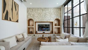 A modern living room with a stone wall, a mounted TV, and a large window with curtains. - Villa Tora Canggu (Canggu)