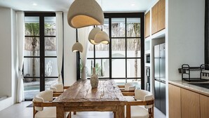 A modern kitchen with a wooden dining table, white chairs, a large window with a view of palm trees, and a built-in refrigerator. - Villa Tora Canggu (Canggu)