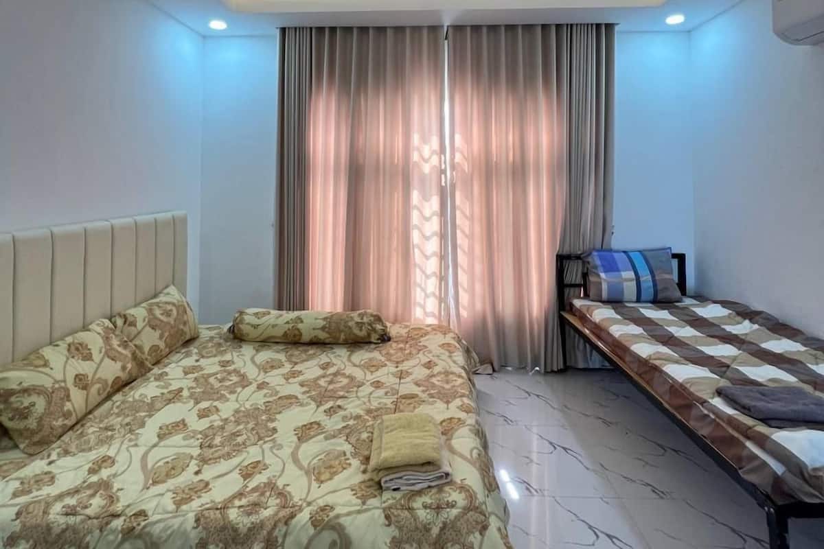 A bedroom with a large bed, a smaller bed, a bench, and a window with curtains.