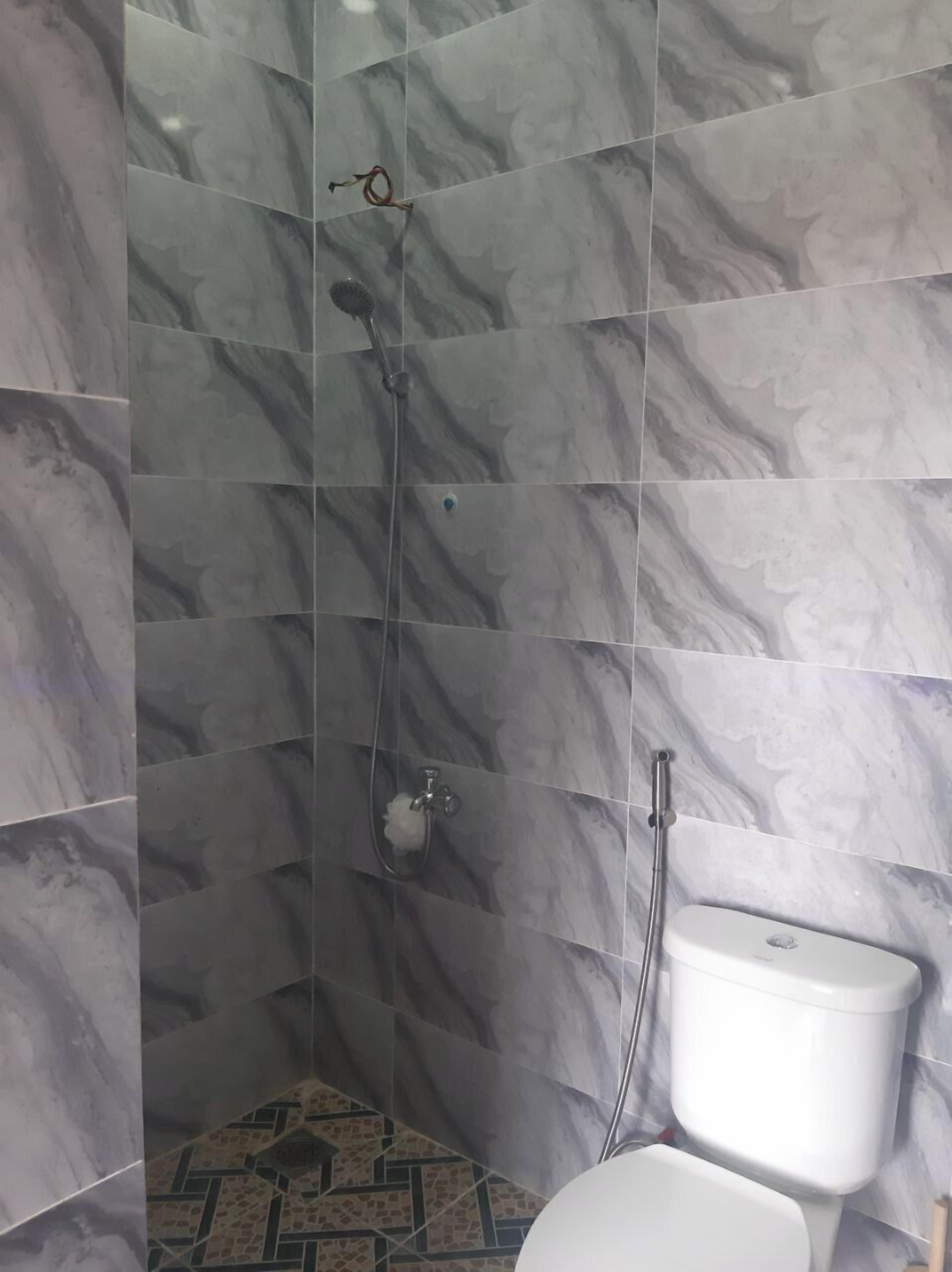 Un baño con azulejos de mármol, ducha e inodoro.