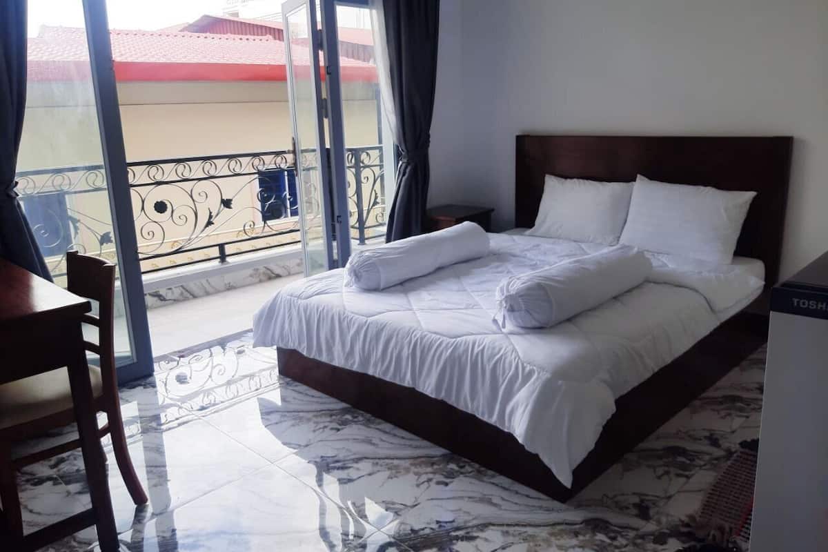 A hotel room with a bed, a chair, and a view of the outside.