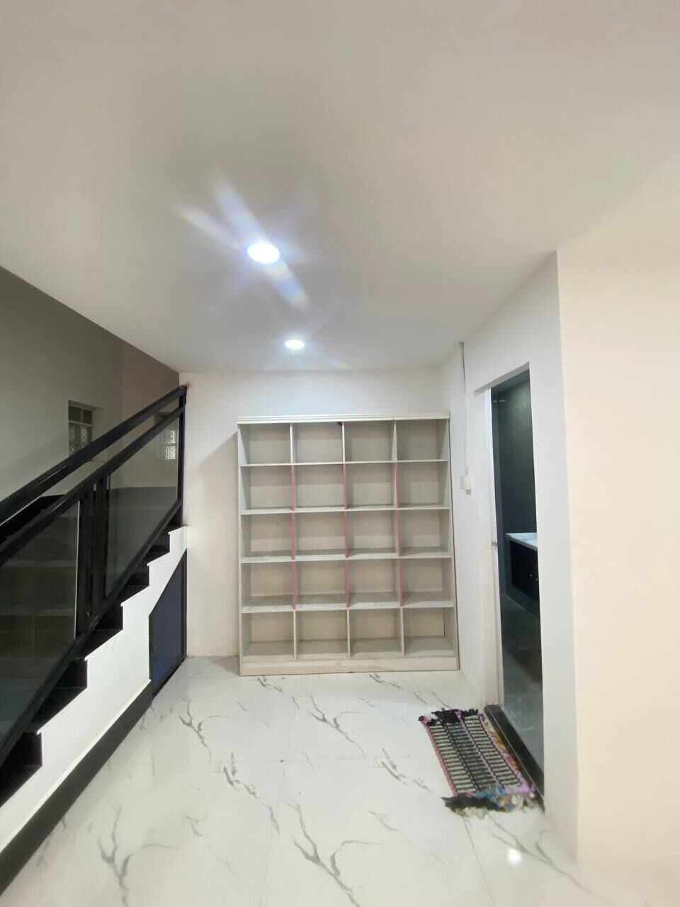 A spacious hallway with a marble floor, a staircase with black railings, and a large built-in shelving unit.