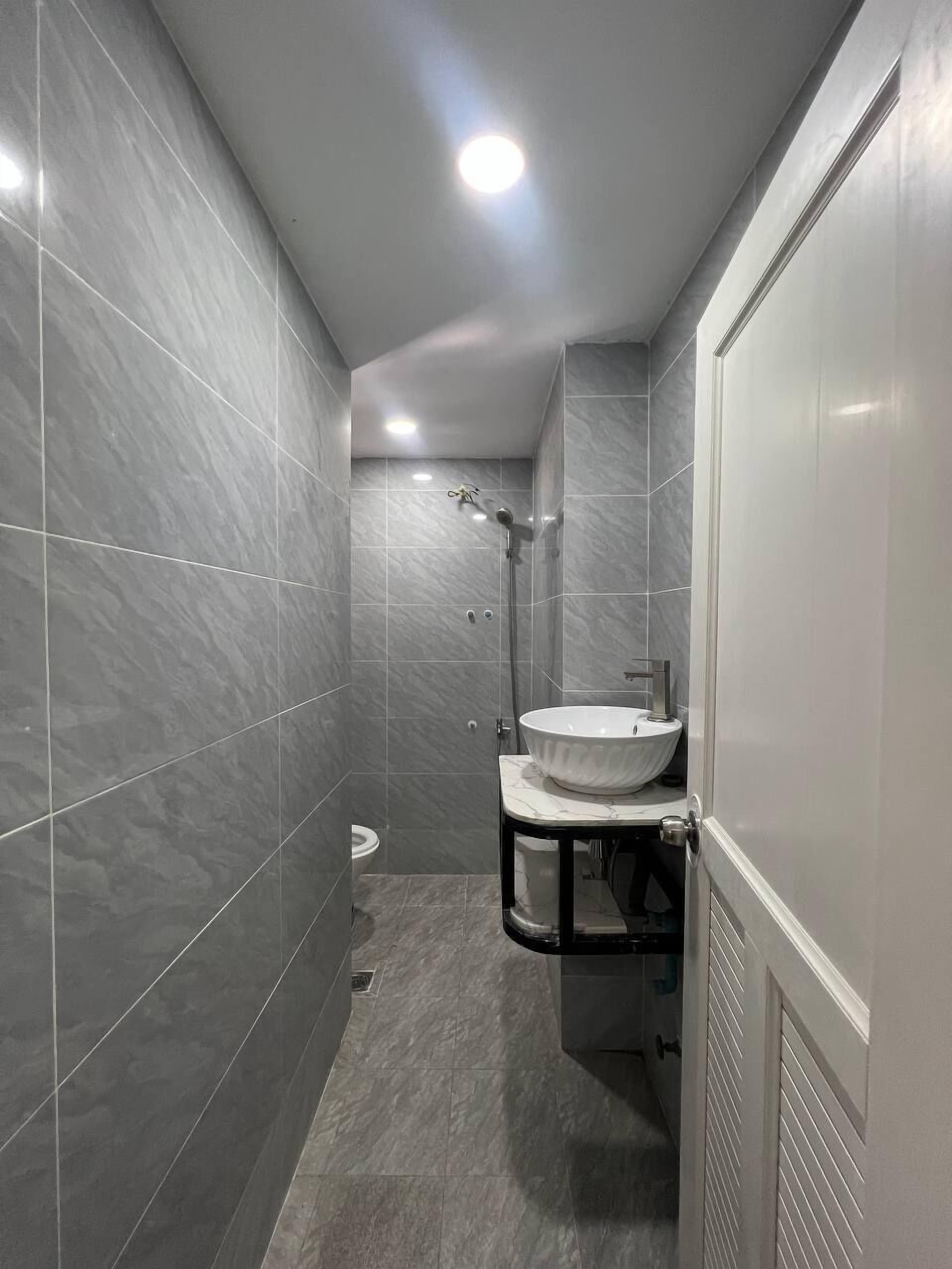 A modern bathroom with grey tiles, a white sink, and a shower.