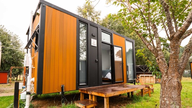A modern, compact cabin with a wooden exterior and large glass windows.