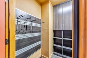 Un couloir avec un portant en métal pour suspendre des vêtements, une porte en bois et une armoire dotée de plusieurs étagères.