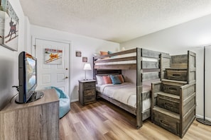 Une chambre avec un lit superposé, un bureau avec un ordinateur, une lampe et une porte ornée d’une affiche.