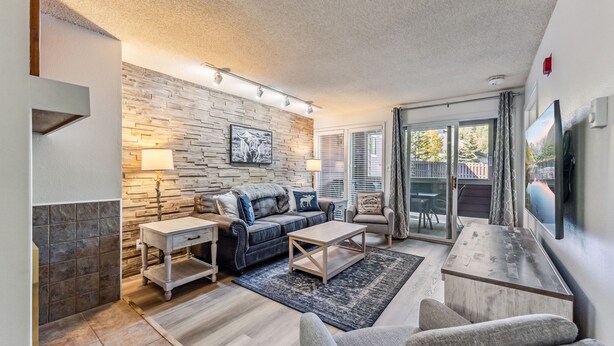 A modern living room with a stone wall, a sofa, a coffee table, and a TV. - Steps to Gondola, Ski-In, 1 Block Main St, Hot Tub (Breckenridge)