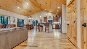 A spacious living room with a wooden ceiling, a large sofa, and a dining area with chairs and a bar. - Kings Beach Retreat: Hot Tub, Walk to Beach (Kings Beach)