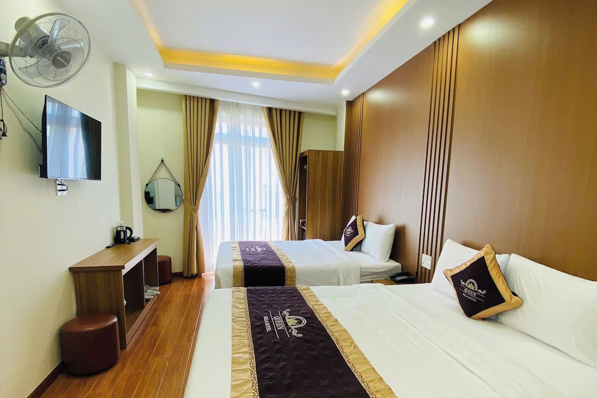 A hotel room with two beds, a TV, a desk, and a fan.