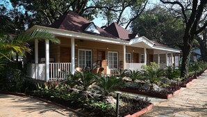 A two-story house with a covered porch, large windows, and a garden with various plants and a small water feature. - Neelam Foresteria Resort (Pipariya)