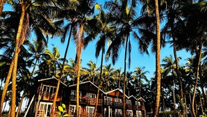 Un resort con diverse cabine di legno circondate da alte palme e un cielo azzurro terso.