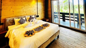 Camera da letto in una baita di legno, con un letto grande, una ventola a soffitto e vista su una terrazza esterna.