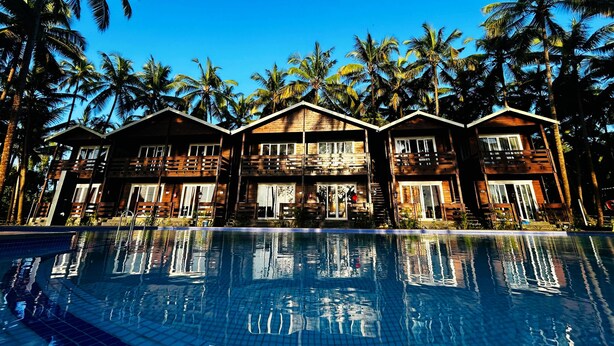 Un resort con cabine in legno, piscina e palme.