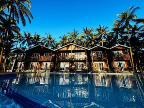 A resort with wooden cabins, a swimming pool, and palm trees. - Seclude Eco Cottages (Anjuna)