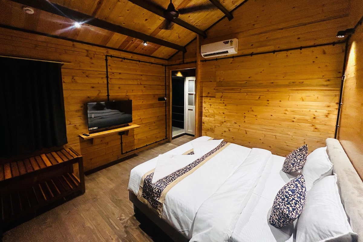 A wooden cabin room with a bed, a TV mounted on the wall, and a ceiling fan.