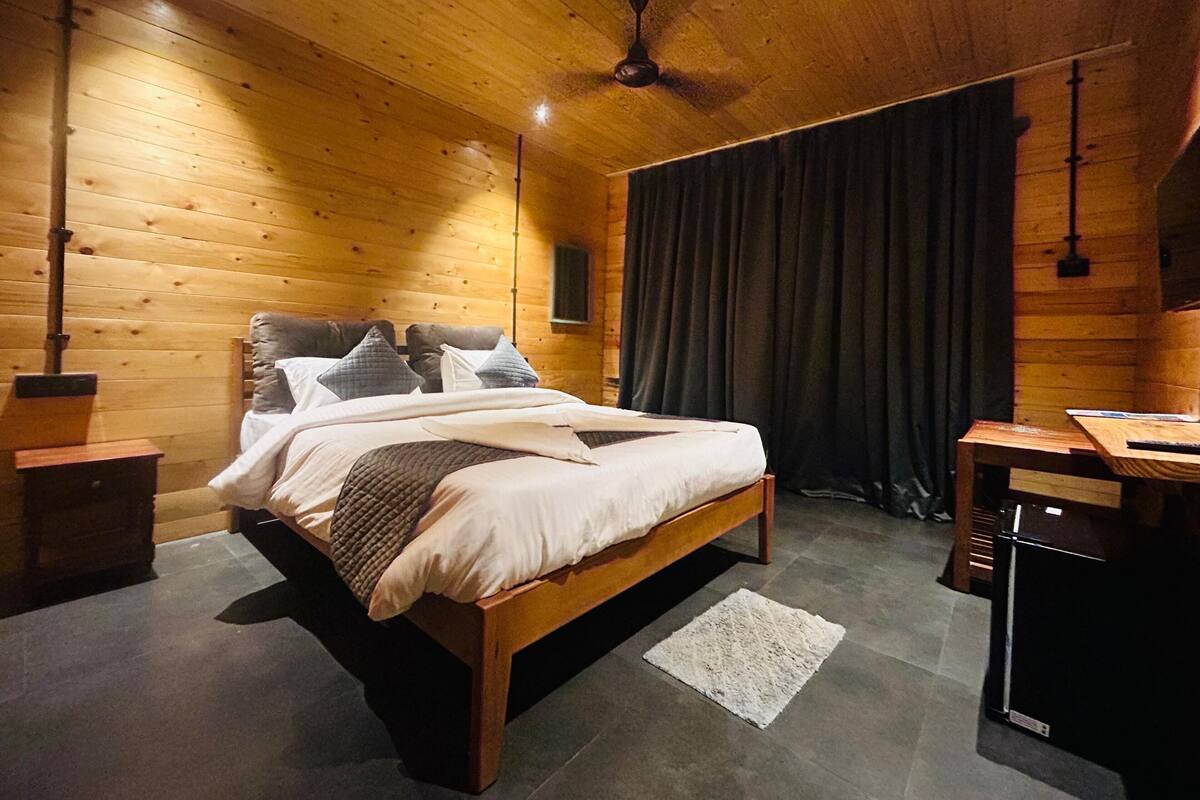 A wooden-paneled bedroom with a bed, bedside tables, a ceiling fan, and a large window with curtains.