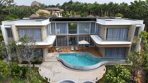 Une maison moderne à plusieurs étages, dotée d’une grande piscine, d’un espace extérieur aménagé et d’une végétation luxuriante.