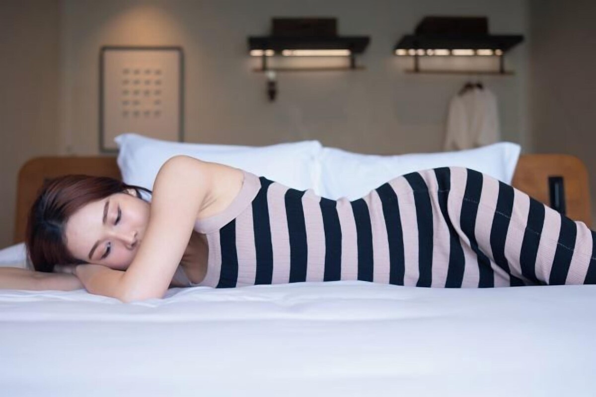 A hotel room with a bed, pillows, a headboard, and a wall-mounted light fixture.