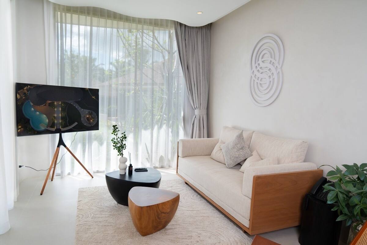 A modern living room with a large flat-screen TV on a stand, a beige sofa, a round coffee table, and a wooden side table.