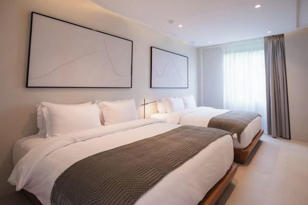 A hotel room with two beds, a large window with curtains, and abstract wall art.