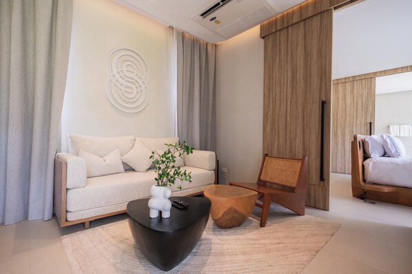 A modern living room with a sofa, a coffee table, a wooden chair, and a bed. - Mahutsachan Klong Thom (Khlong Thom)