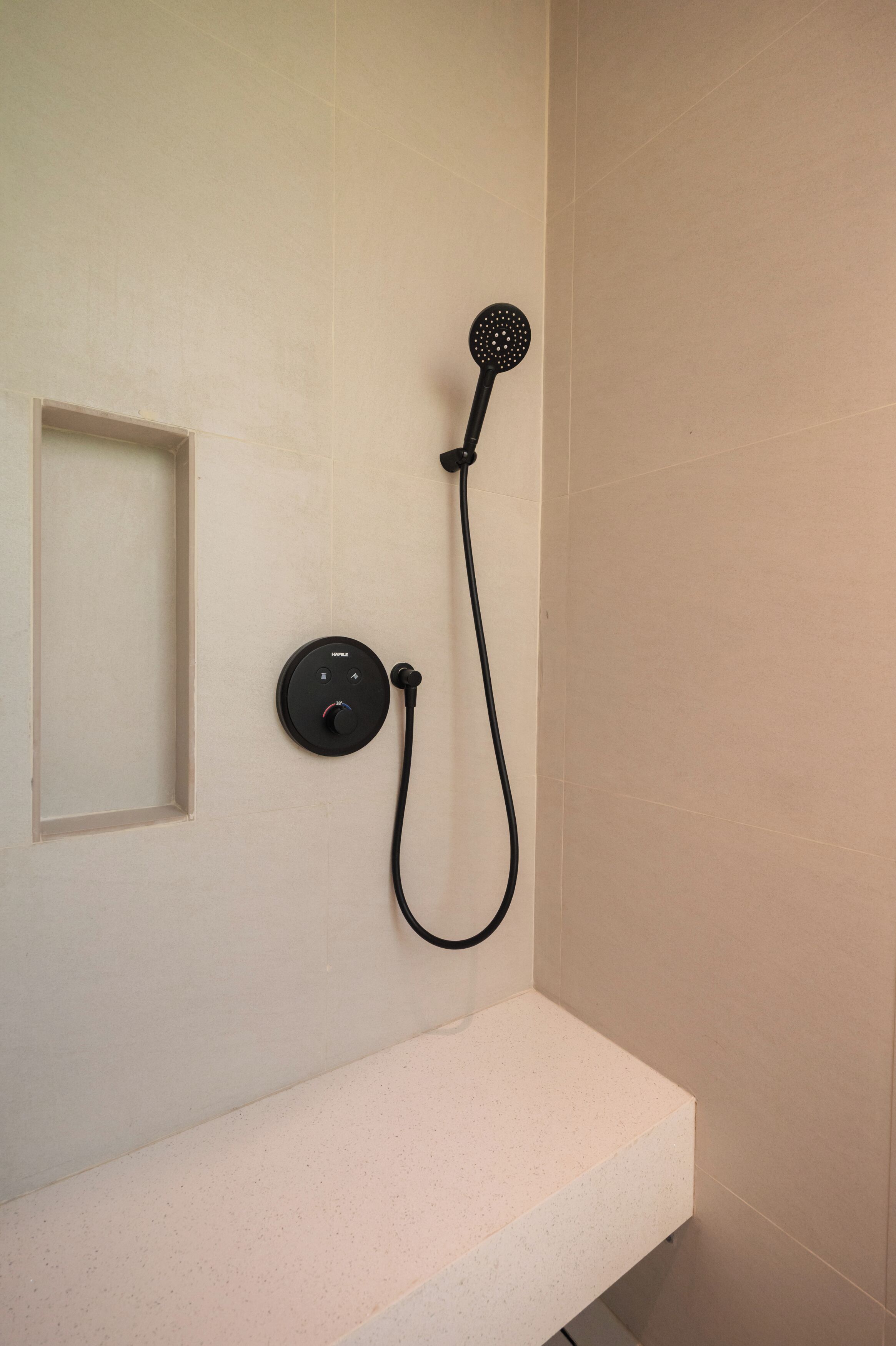 Een badkamer met een wit aanrechtblad, een zwarte handdouche en een bedieningspaneel.