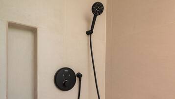 Een badkamer met een wit aanrechtblad, een zwarte handdouche en een bedieningspaneel.