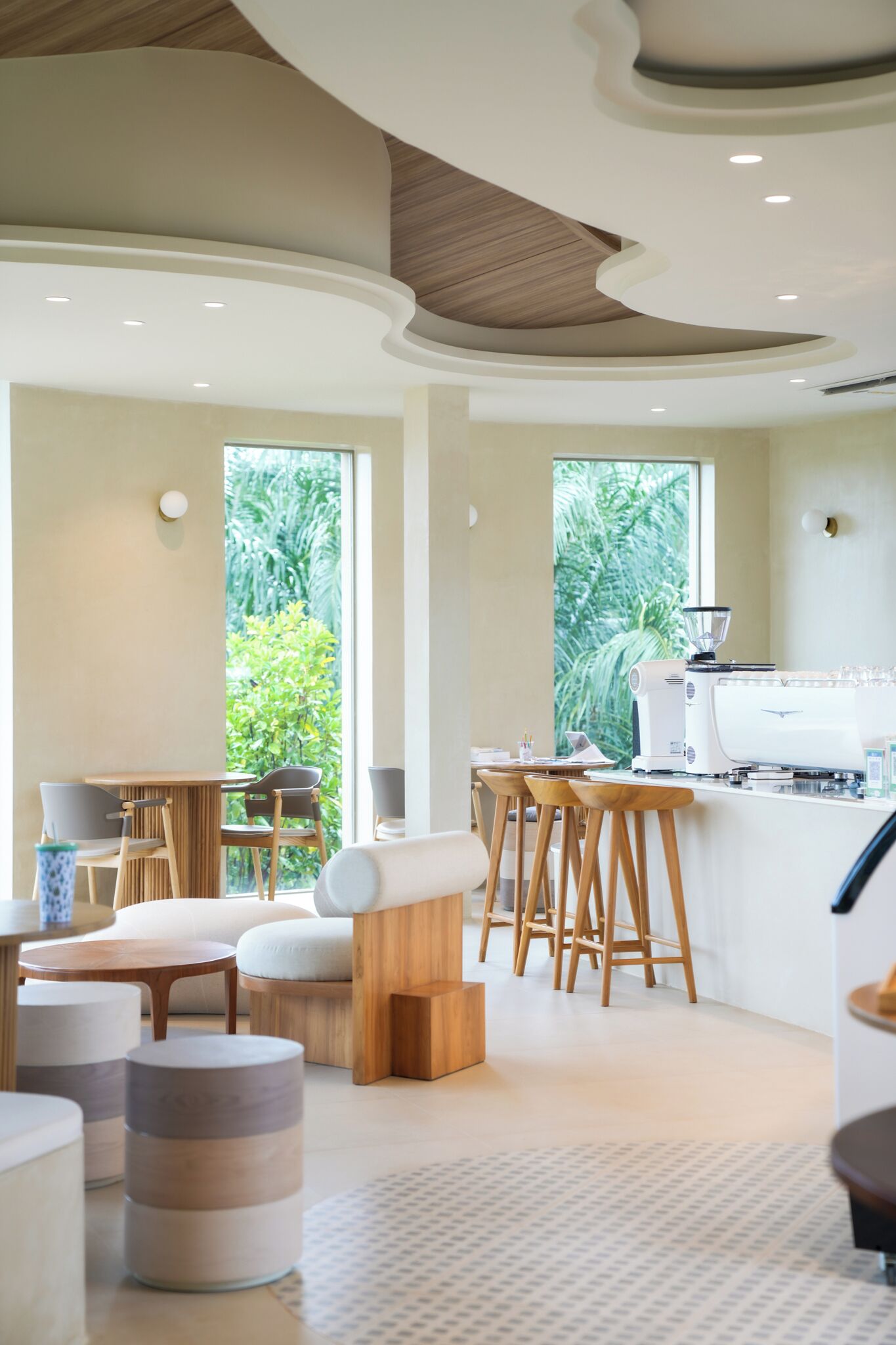 A modern kitchen with a coffee machine, bar stools, and a view of greenery outside.