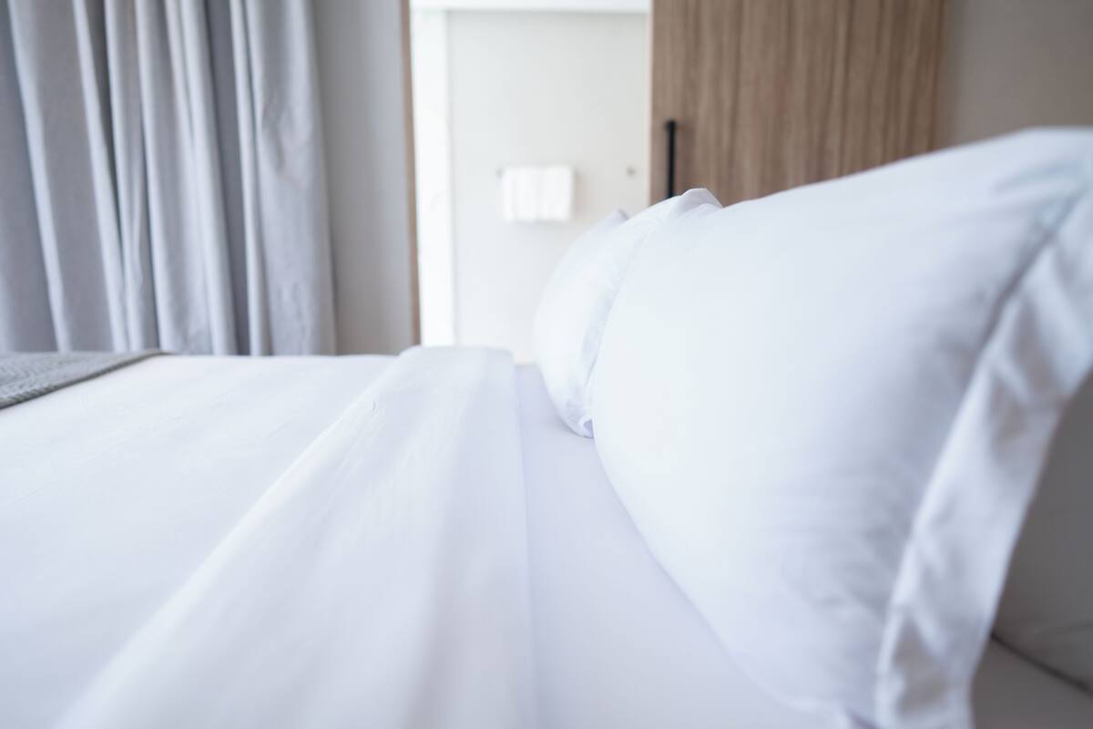A hotel room with a neatly made bed, a visible door, and a curtain.