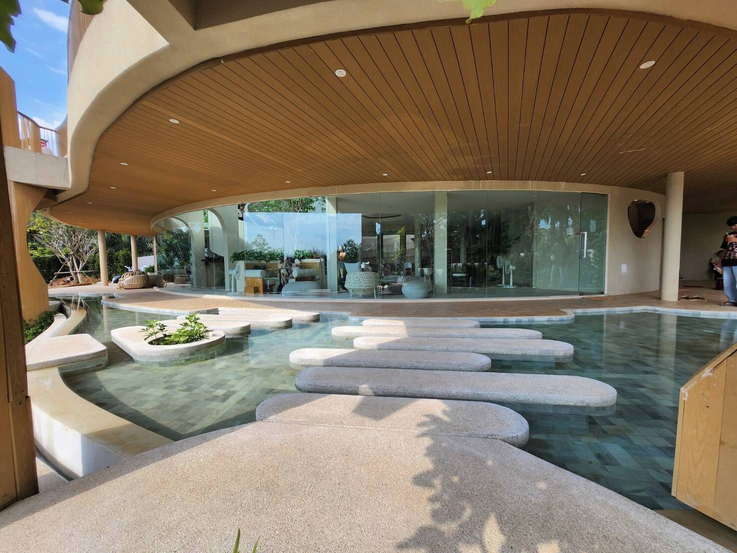 A modern building with a curved wooden ceiling, a glass facade, and a pool area with stone steps.